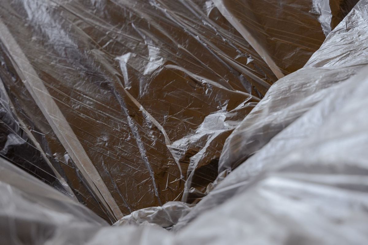Heavy clear plastic sheeting laid loosely over a wood floor, the kind of thin barrier that a proper sealed liner replaces
